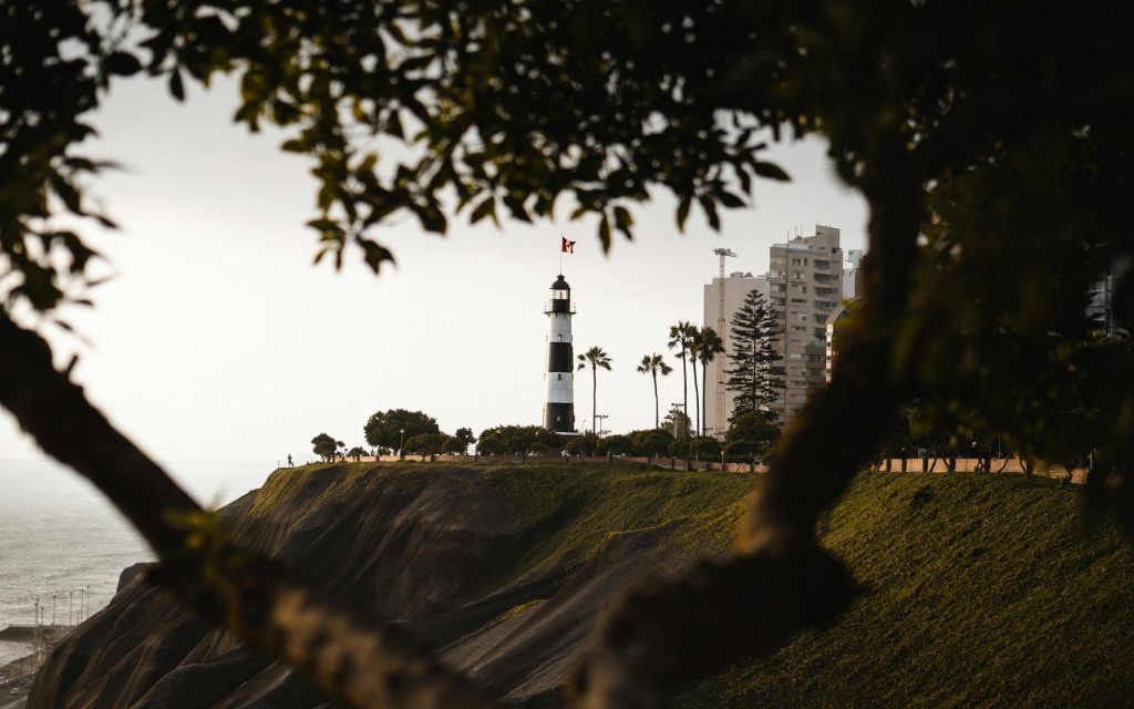 A scenic view of a lighthouse surrounded by trees and buildings atop ocean cliffs.