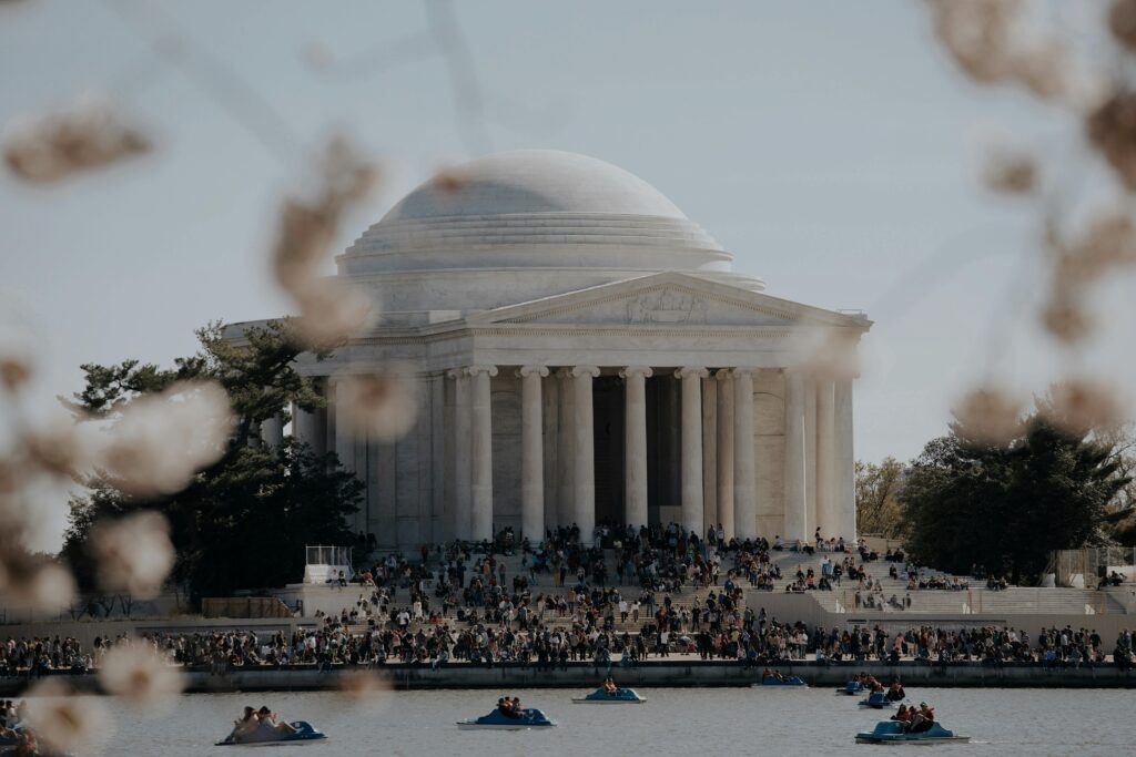 Crowds enjoying a sunny day at the Jefferson Memorial with cherry blossoms in bloom.